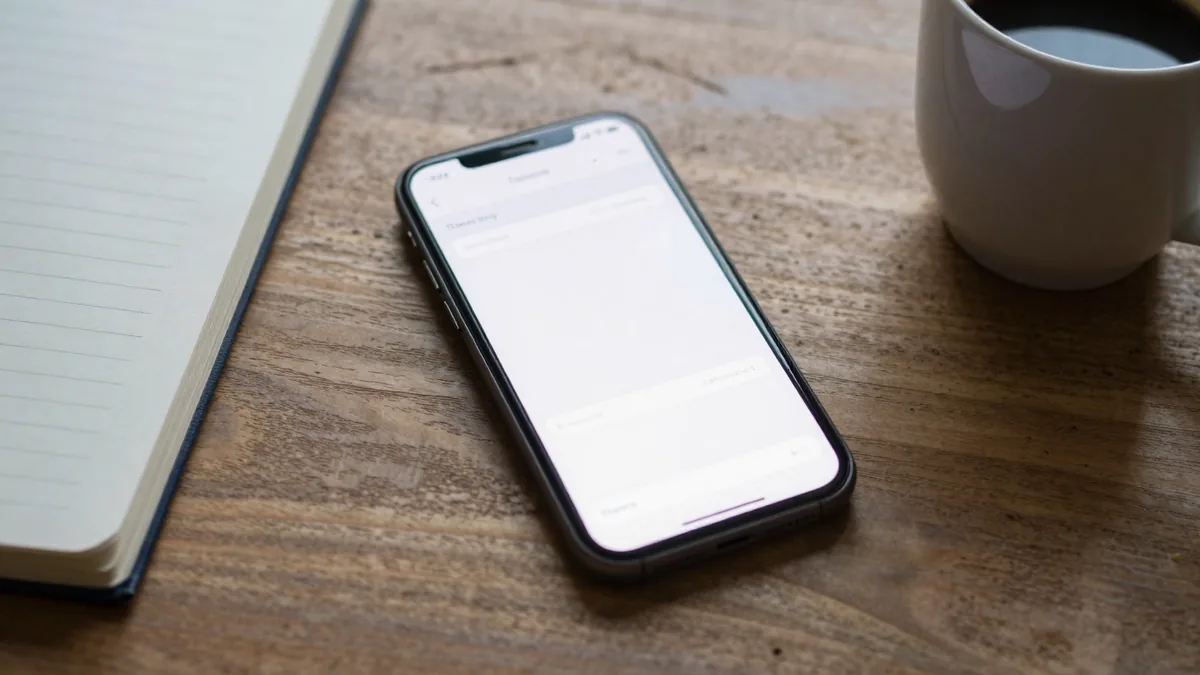 木のテーブルに置かれたスマートフォンとノートのイメージ画像